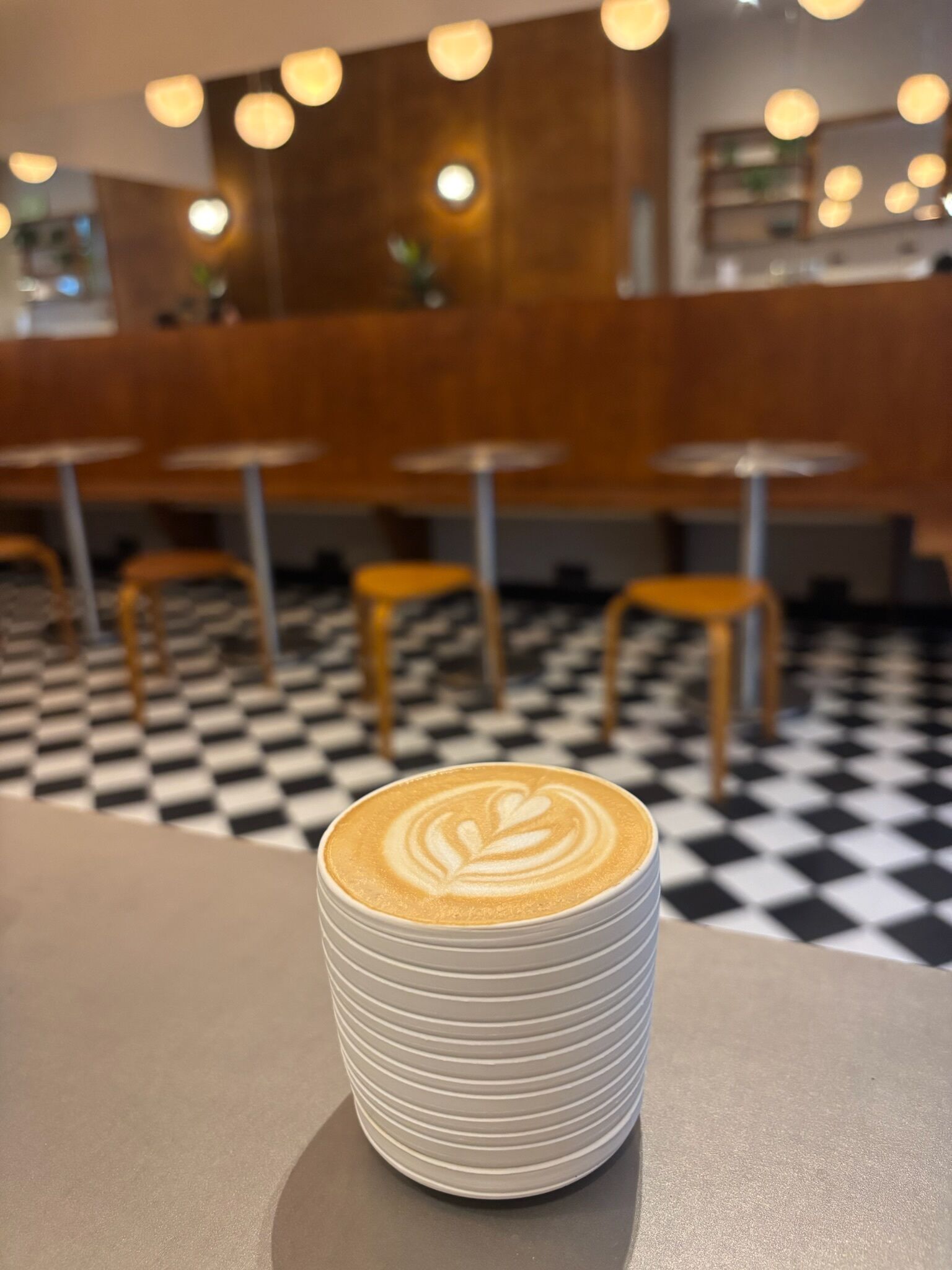 A coffee cup with latte art on a table in a cafe with checkered flooring and wooden chairs.