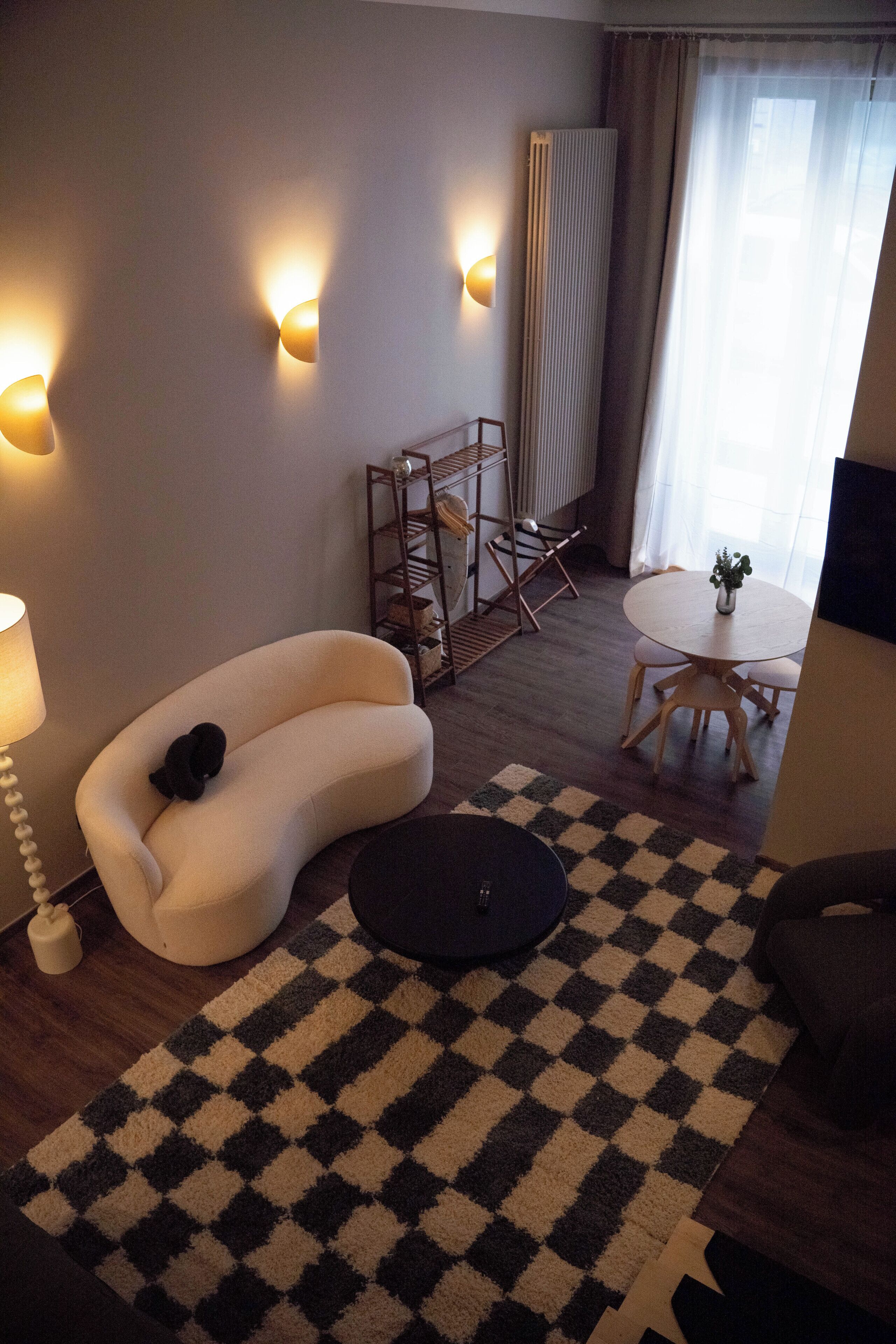 Una sala de estar moderna con un sofá, una mesa redonda, un tapete a cuadros y luces fijadas a la pared.