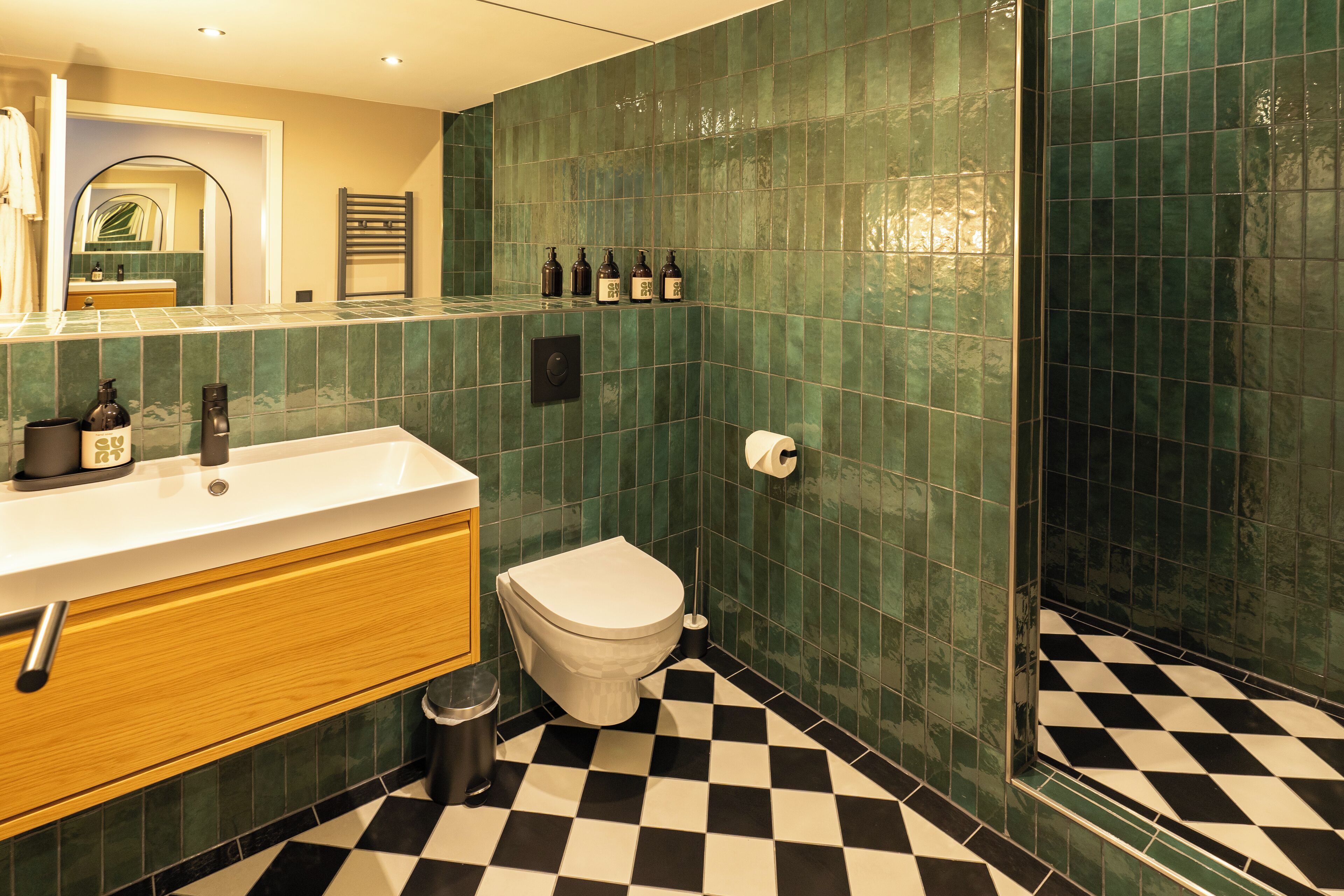 A bathroom with a checkered floor, a toilet, a sink with toiletries, and a mirror.