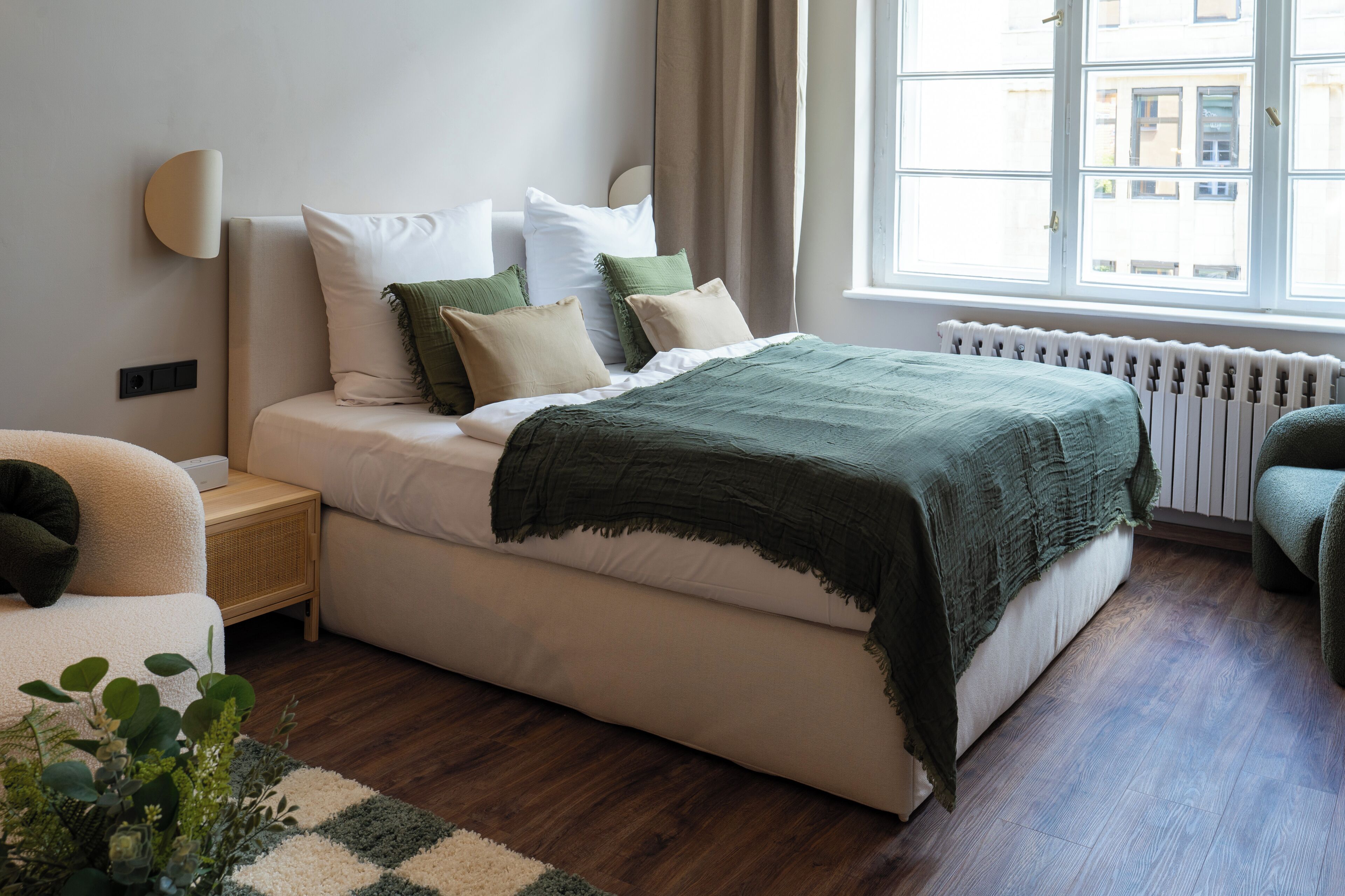 A bedroom with a bed, bedside table, lamp, and a window with a view of buildings.