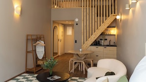 A modern interior with a wooden staircase, a dining area with a round table and chairs, a coat rack, and a small kitchen area. - The Charming by Curt Suites (Berlin)