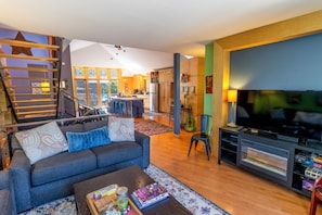 Una sala de estar moderna con sofá, mesa de centro, televisor, chimenea y cocina al fondo.