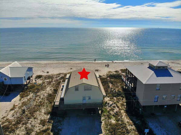A beachfront property with a prominent red star on the roof of the central building, surrounded by sandy terrain and a view of the ocean.