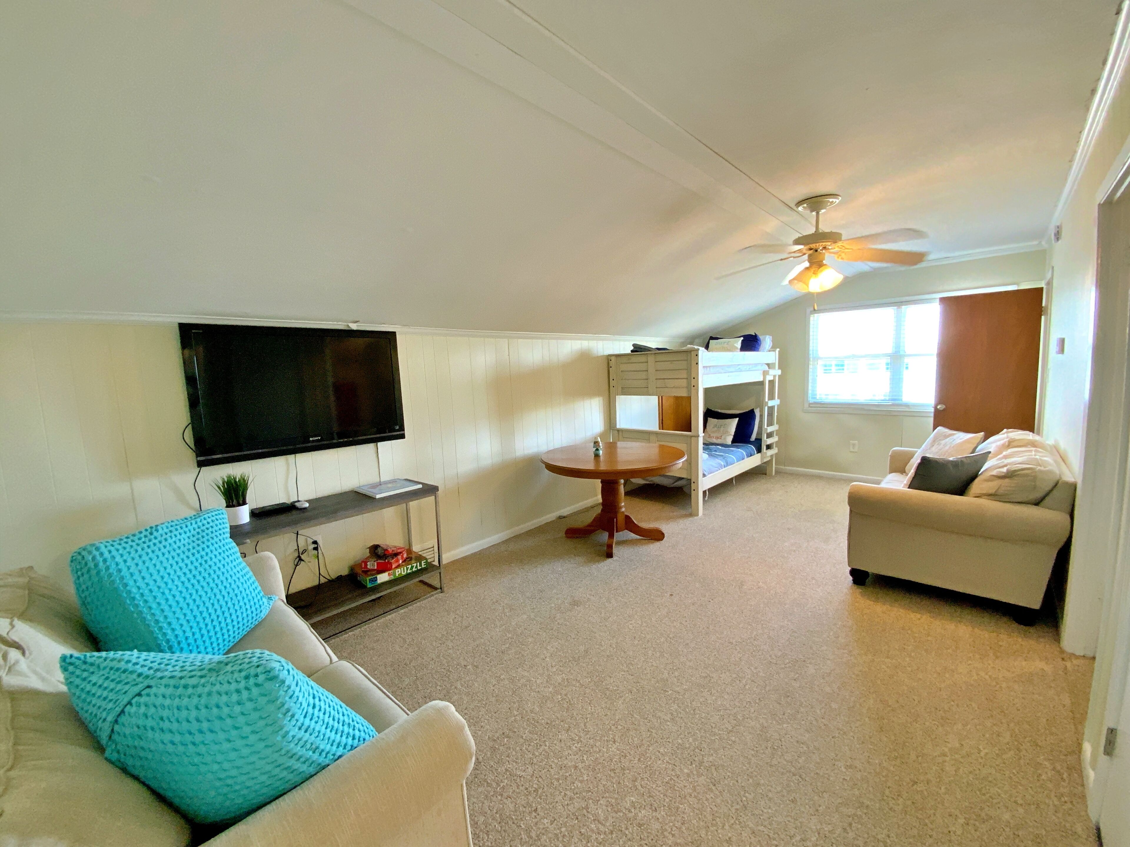 A living room with a TV, a sofa, a coffee table, a bunk bed, and a ceiling fan.