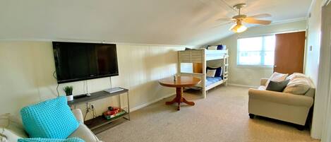 A living room with a TV, a sofa, a coffee table, a bunk bed, and a ceiling fan.