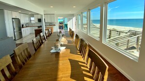 A long dining table with chairs, a kitchen area, and large windows with a beach view. - Beachfront in Surfside Shores (Gulf Shores)