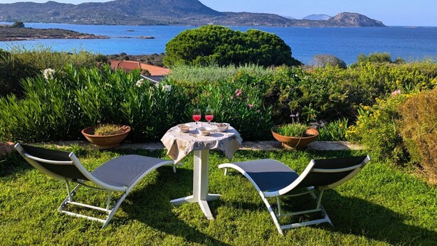Ein Garten mit Tisch und Stühlen, Blick auf das Meer und Berge im Hintergrund.