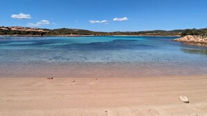 Ein Strand mit klarem Wasser, sandigem Ufer und sanften Hügeln im Hintergrund.