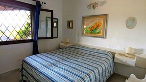 Ein Schlafzimmer mit Bett, Fenster mit Vorhang, Nachttisch und einem Spiegel.