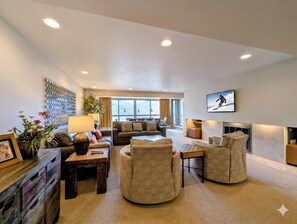 A modern living room with a fireplace, a large window, and a mounted TV.