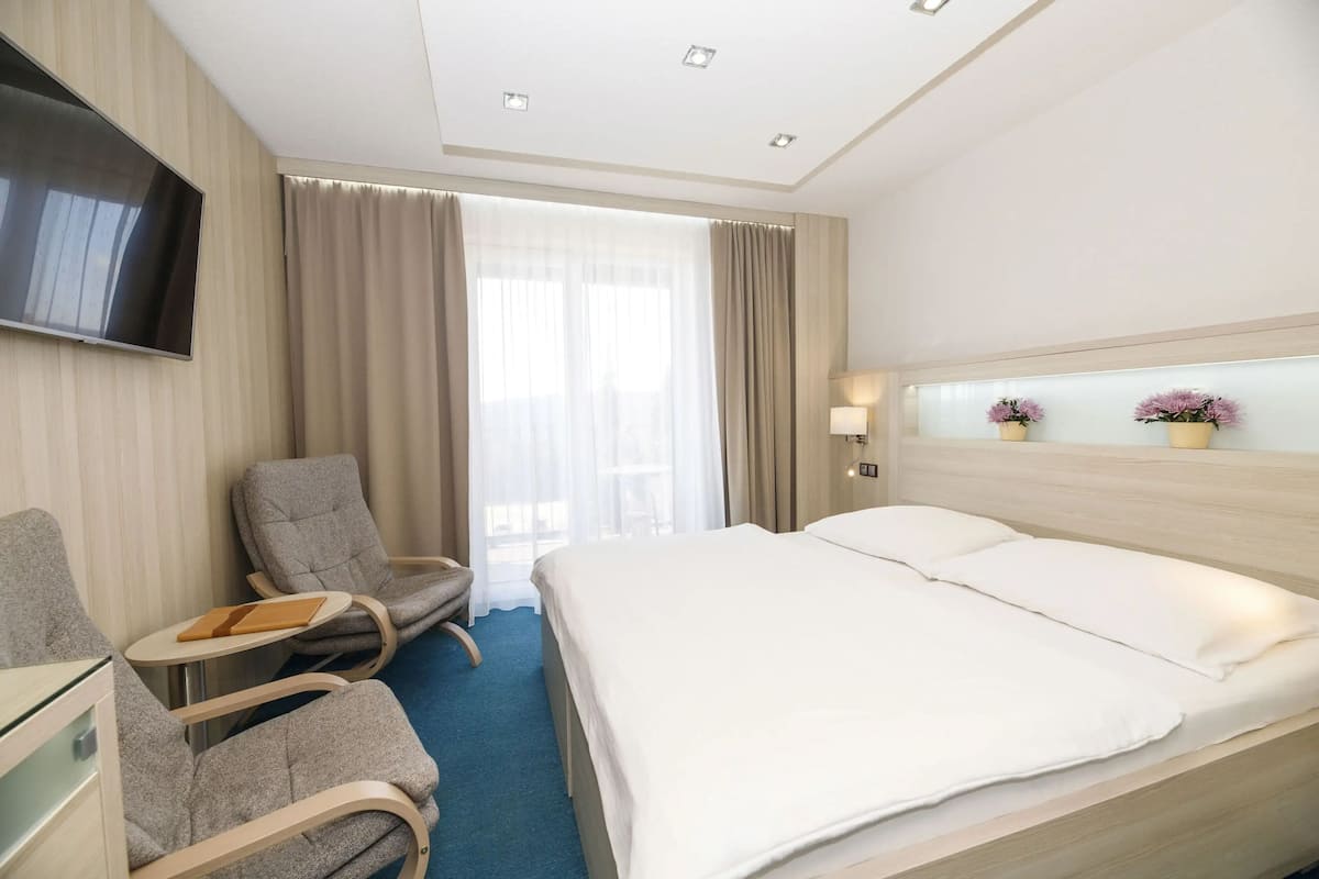 Habitación de hotel con cama, dos sillones, televisión, una mesita y ventana con cortinas.