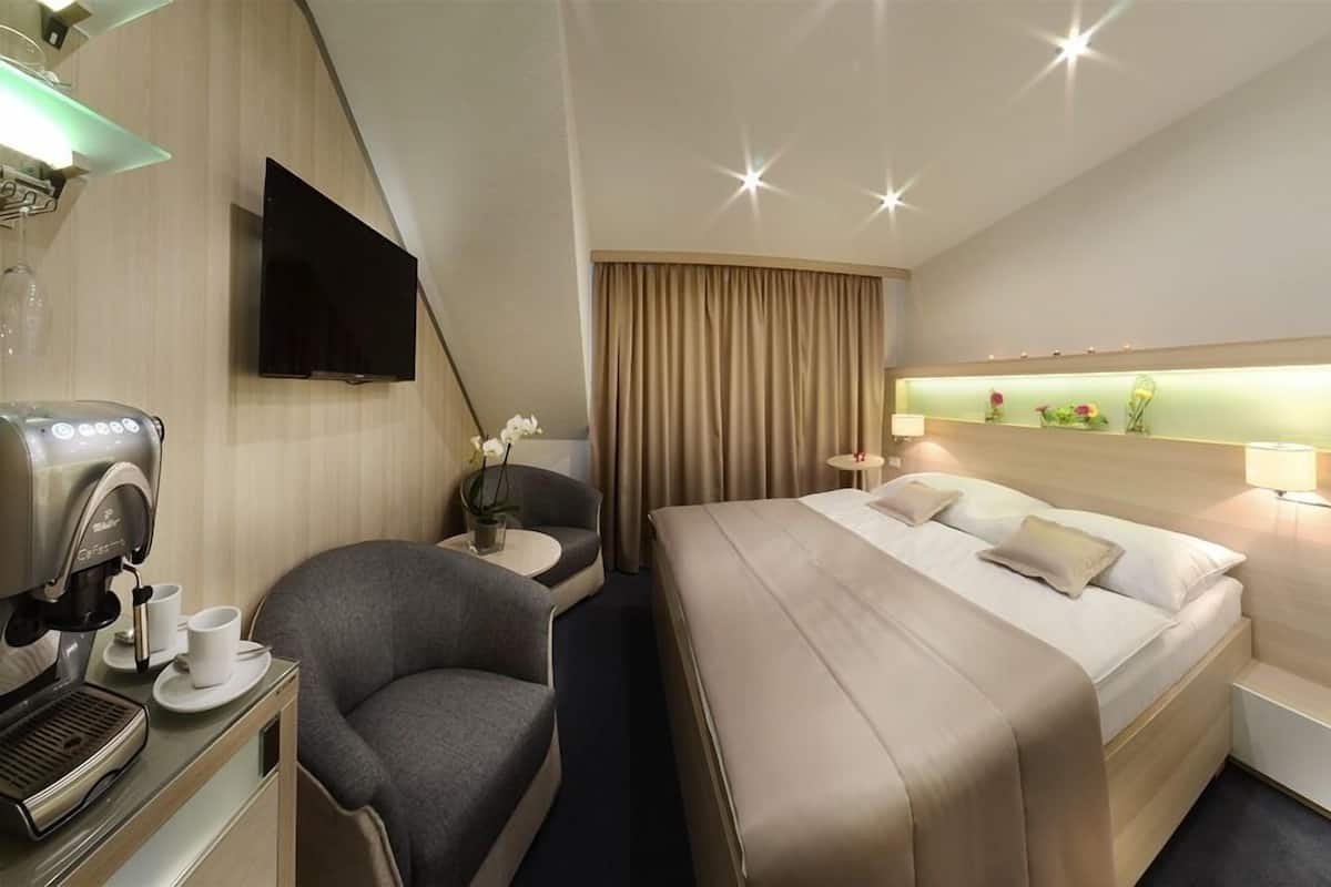 Habitación de hotel con cama, escritorio con cafetera, televisor y un pequeño espacio para sentarse.
