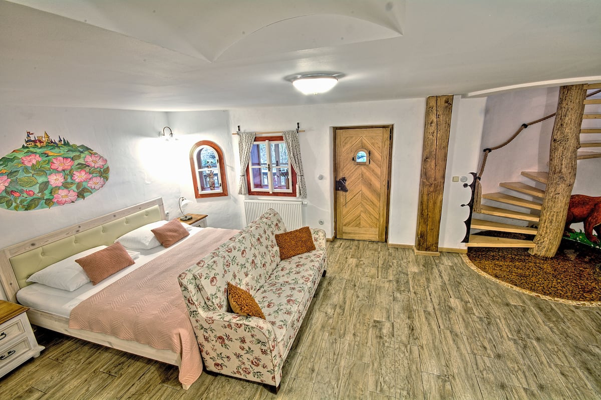 Un dormitorio con cama, sofá, escalera de madera y pared con un mural floral.