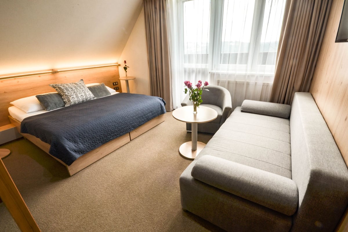 Habitación de hotel con cama, sofá, una mesita redonda y ventana con cortinas.