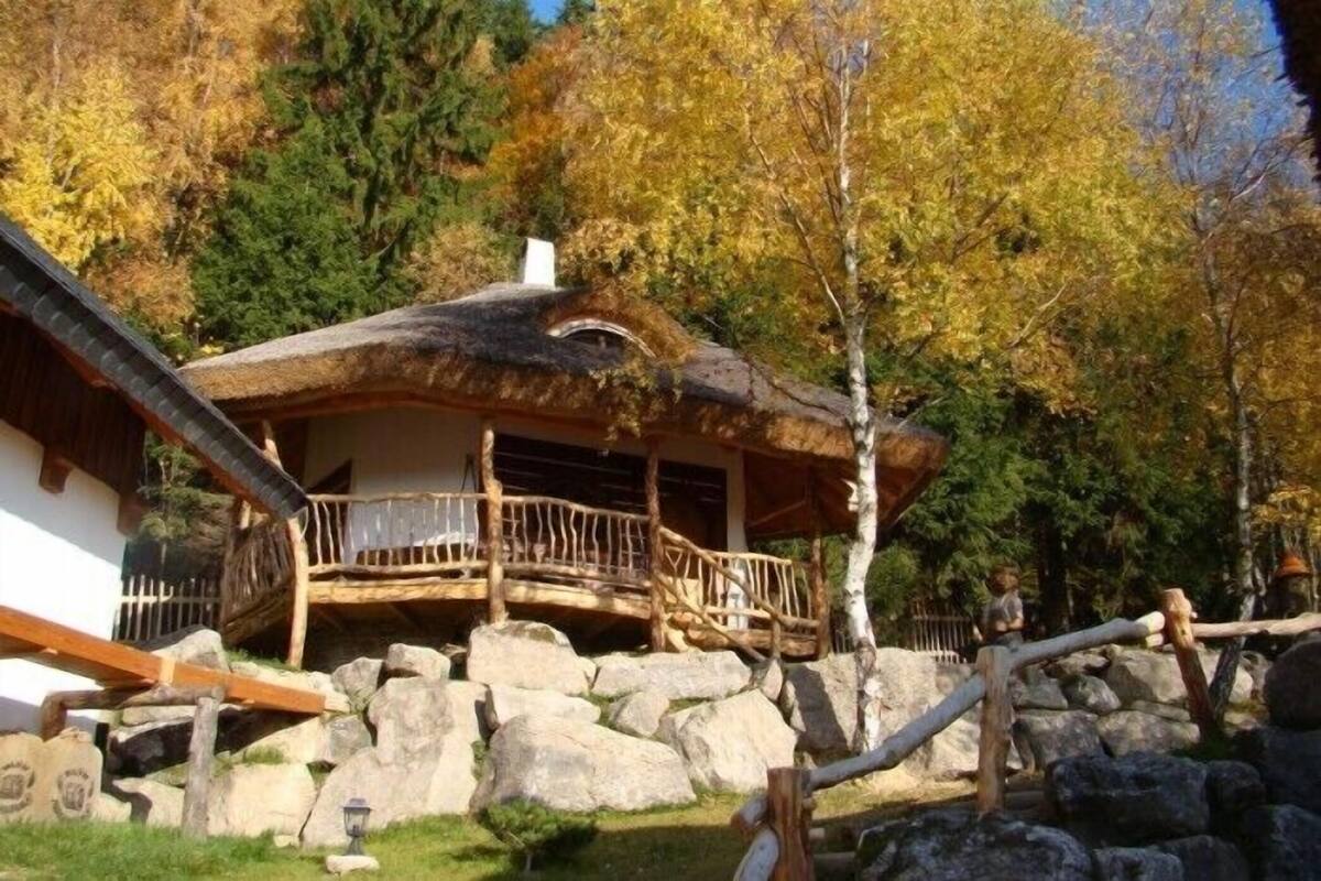 Una cabaña rústica con techo de paja, terraza de madera y base de piedra.