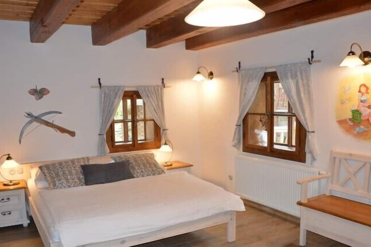 Un dormitorio acogedor con una cama, dos mesitas de noche, un banco de madera y una ventana con cortinas.