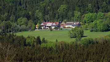 Un edificio grande de varios pisos con un estilo arquitectónico tradicional, rodeado de un bosque denso.