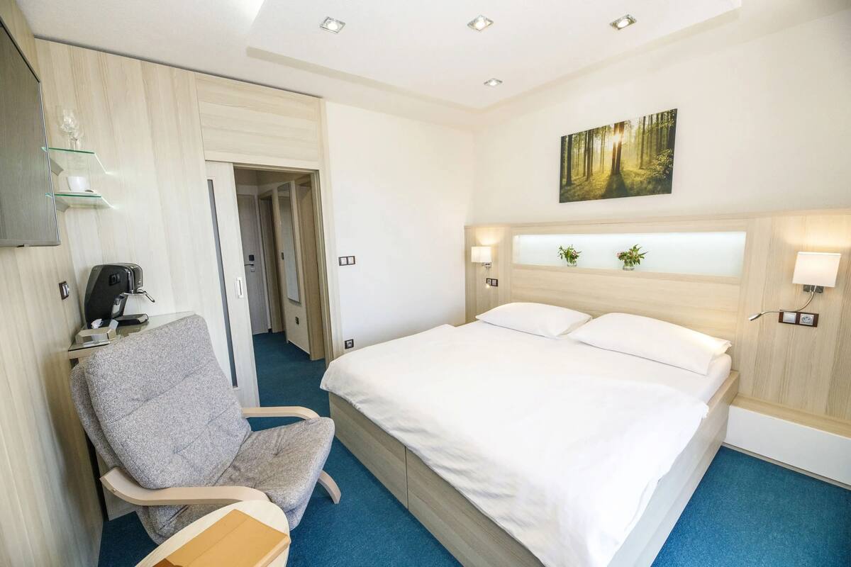 Habitación de hotel con una cama, una silla, un escritorio con una computadora y un cuadro en la pared.