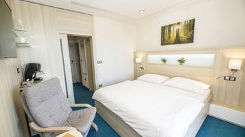 A hotel room with a bed, a chair, a desk with a computer, and a painting on the wall.