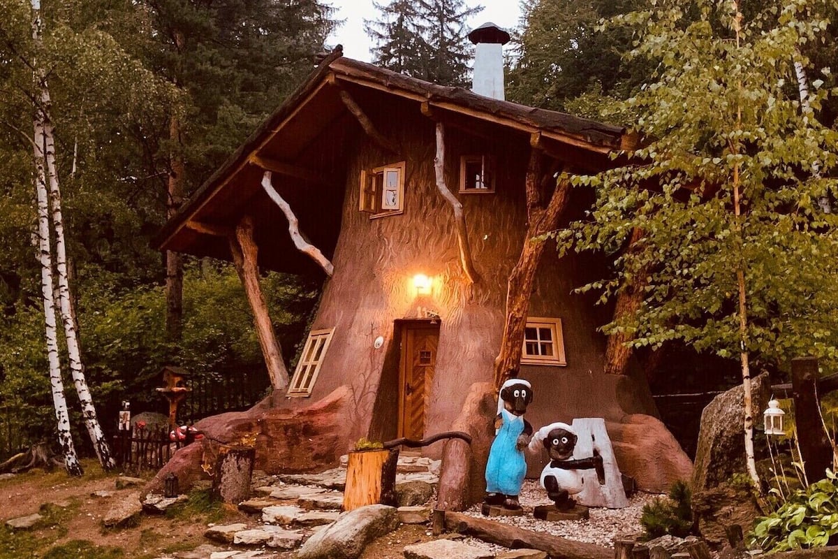 Una casa en un árbol con fachada de madera, una chimenea y un ventanal pequeño.