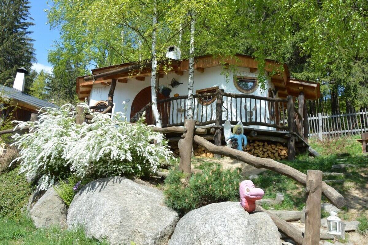Una cabaña rústica con terraza de madera, rodeada de rocas grandes y vegetación.