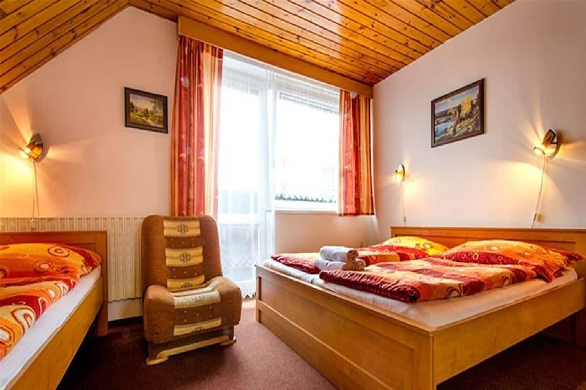 Un dormitorio con techo de madera, dos camas, una silla y dos lámparas de pared.