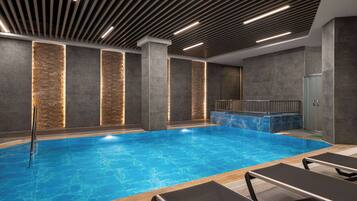 Una piscina interior moderna con superficie de agua azul cristalina, rodeada de sillones de descanso y una pared de piedra con iluminación empotrada.
