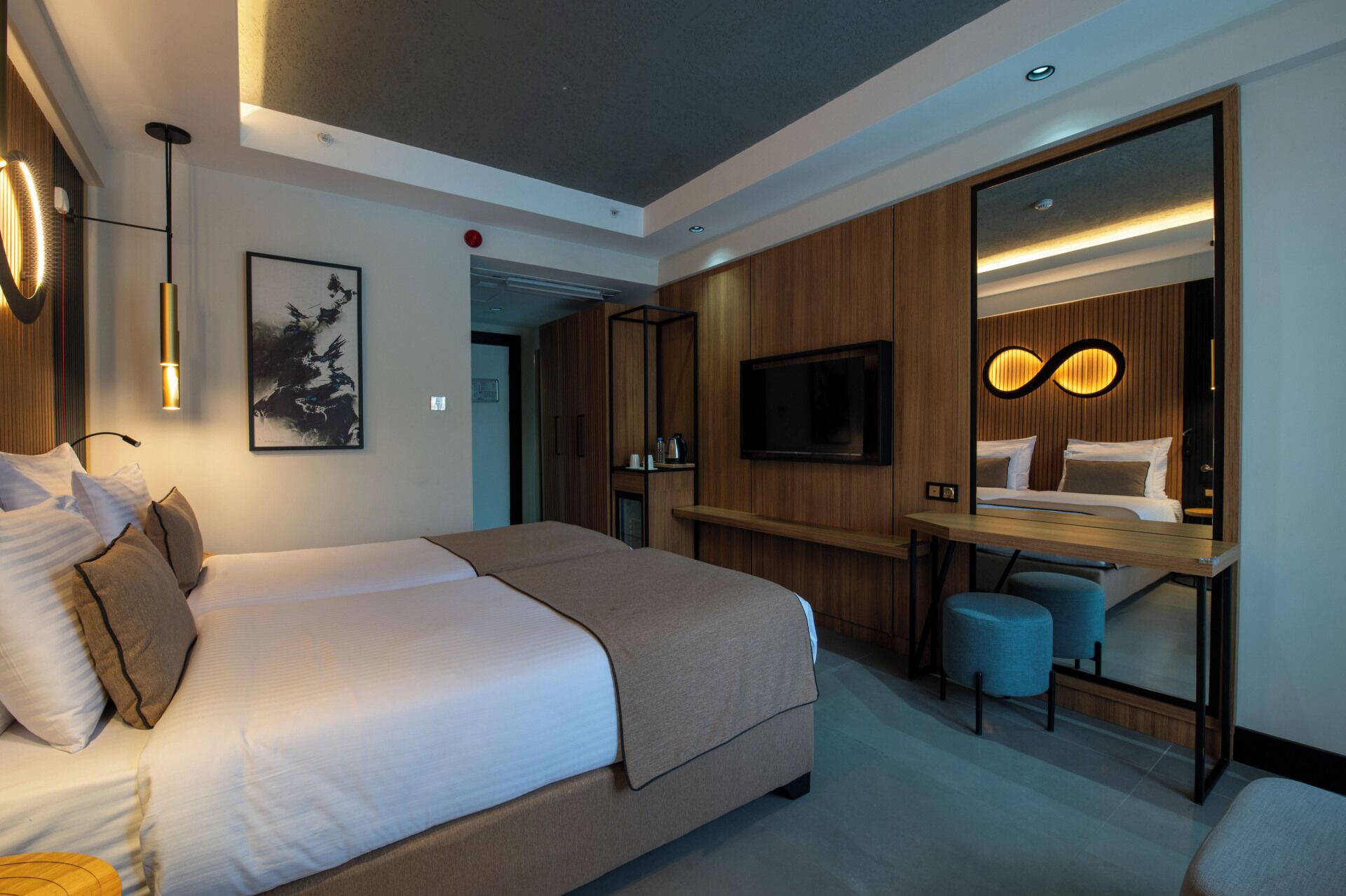 Una habitación de hotel moderna con una cama grande, un escritorio con un televisor de pantalla plana, un espejo y una zona de estar con otomanas.