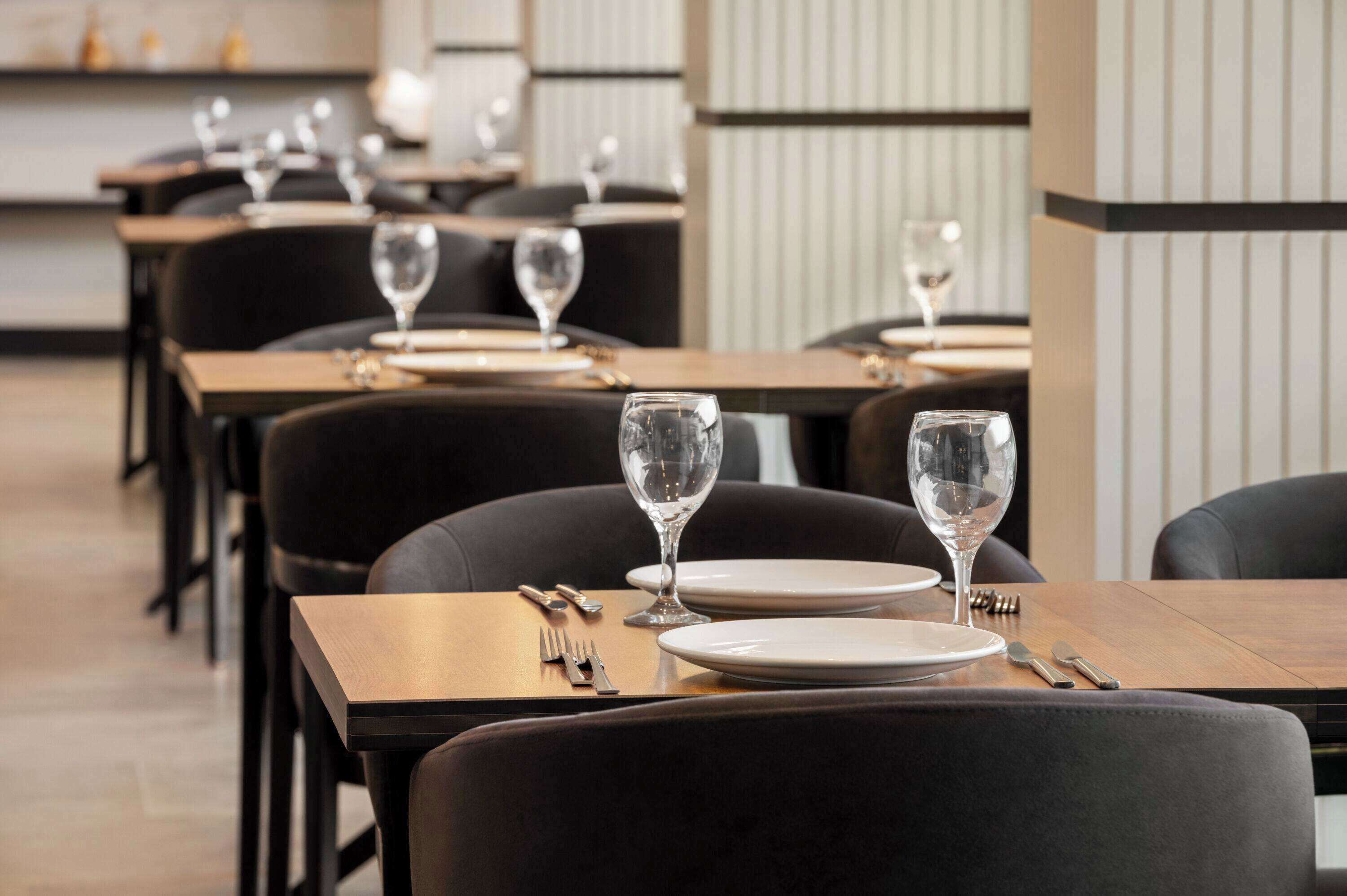 A restaurant with multiple tables, each set with plates, cutlery, and wine glasses.