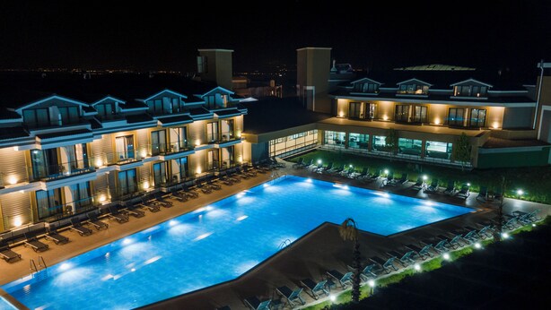 Una piscina grande con tumbonas y un edificio bien iluminado con varios balcones.