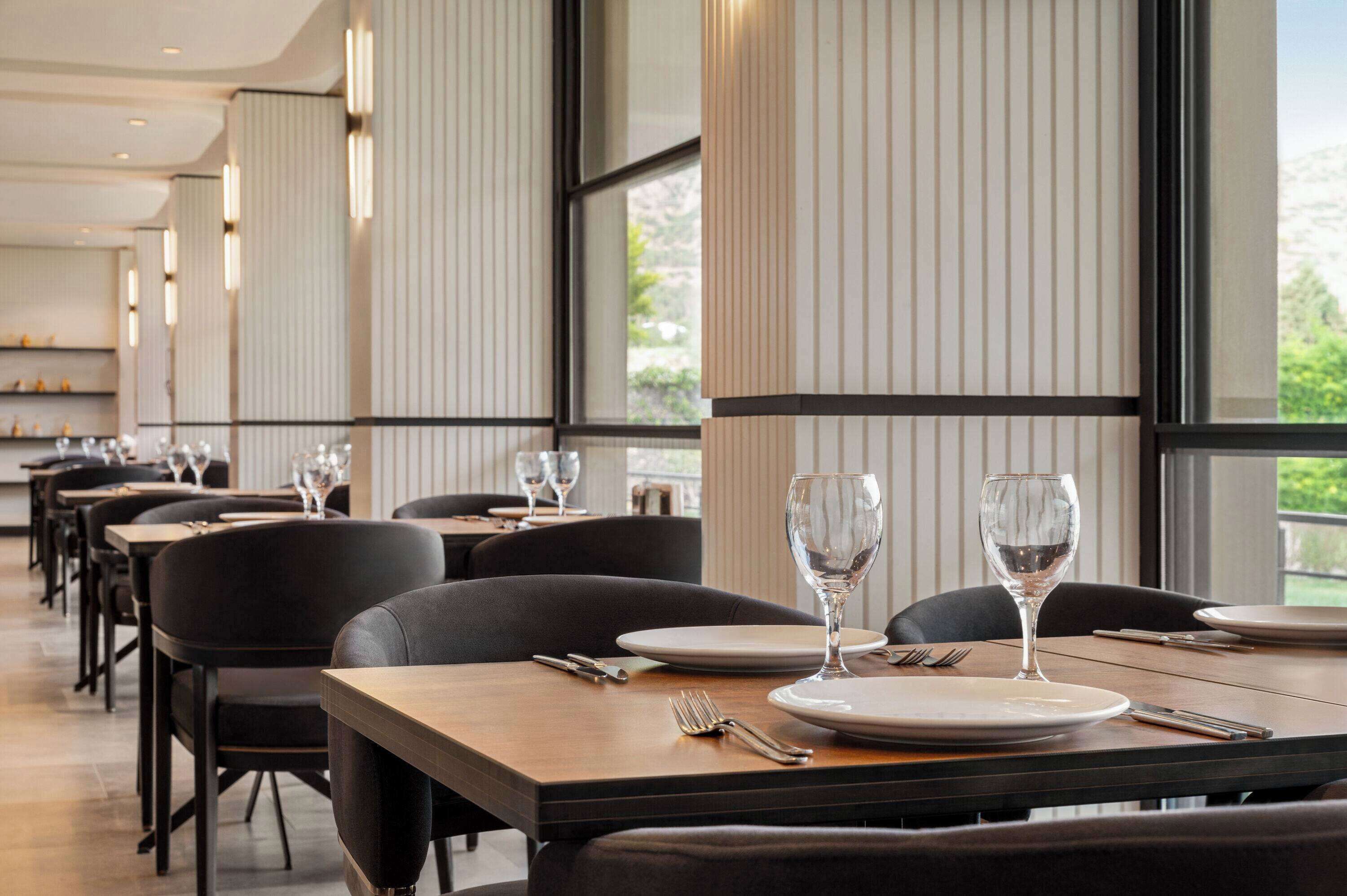 A restaurant with long tables, black chairs, and large windows.