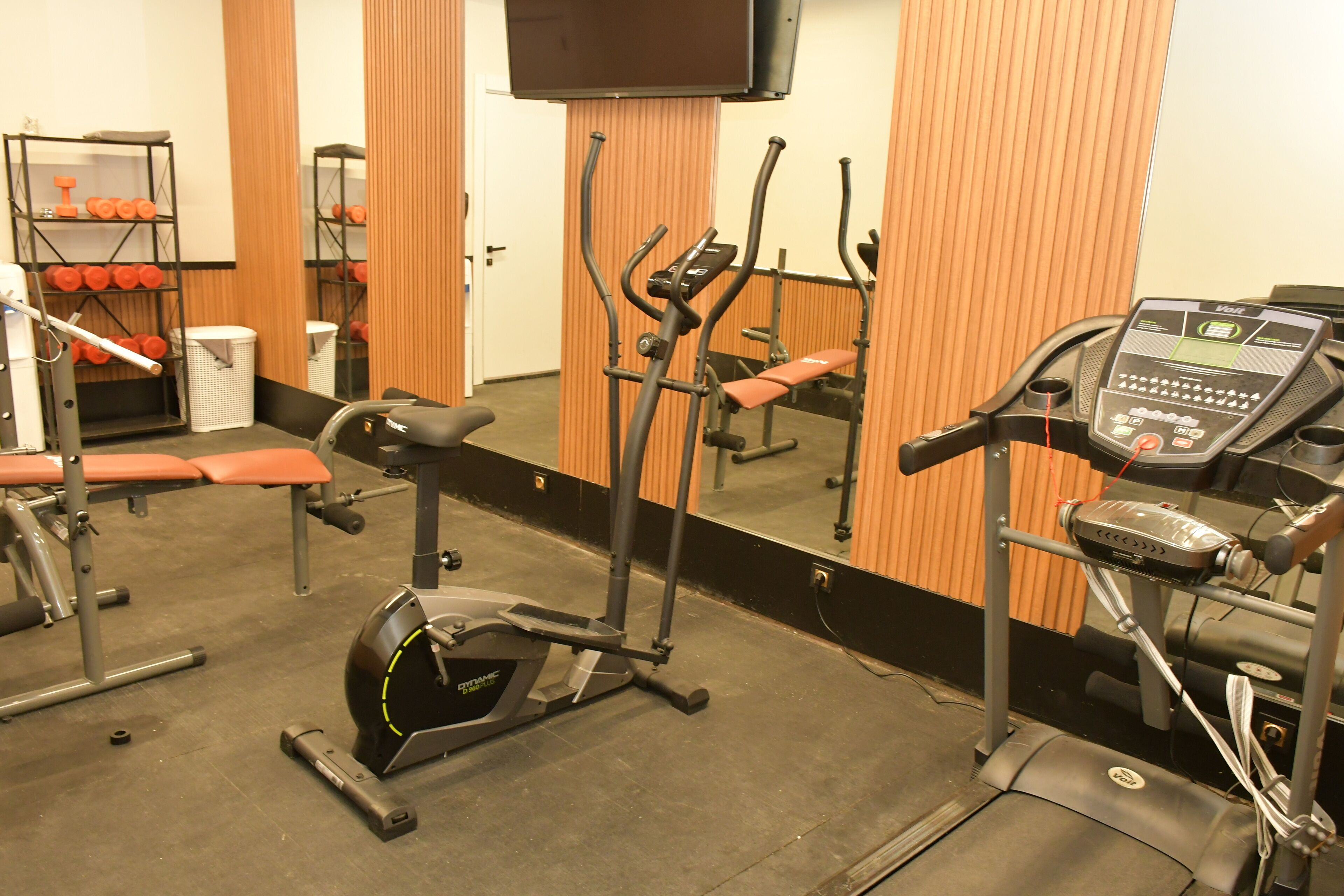A gym with cardio equipment, weight machines, and a TV on the wall.