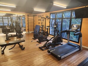 Une salle de sport équipée de divers appareils d’exercice, d’un banc et ornée d’une citation motivante sur le mur.