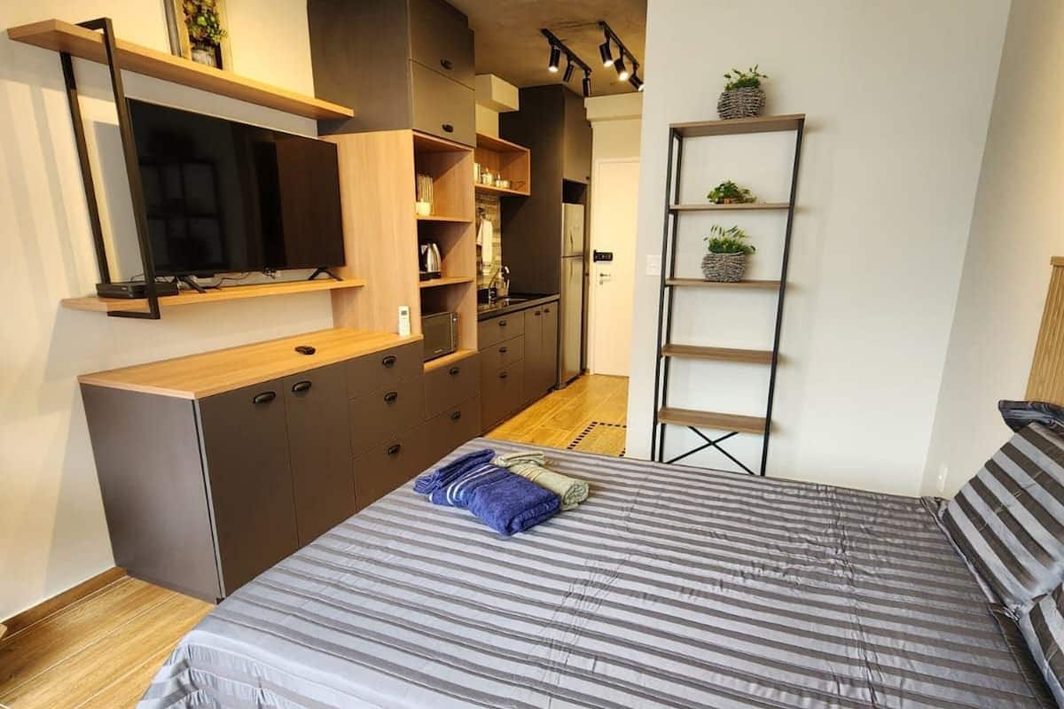 Une chambre à coucher moderne avec un lit, un téléviseur fixé au mur, des placards intégrés et un petit coin cuisine.