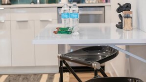 Une cuisine moderne avec des meubles blancs, un plan de travail recouvert de carreaux bleus et un coin repas comprenant une table en verre et des chaises noires.