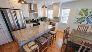 A modern kitchen with a large island, stainless steel appliances, and wooden stools. - M931- Sound Side, Corolla, Saturday Check In, Comm. Pool! (Corolla)