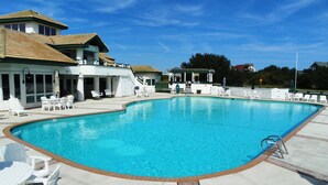 A swimming pool with white lounge chairs and a covered area with tables and chairs. - M931- Sound Side, Corolla, Saturday Check In, Comm. Pool! (Corolla)
