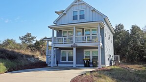 A two-story building with a balcony, a visible address sign, and a trash bin outside. - M931- Sound Side, Corolla, Saturday Check In, Comm. Pool! (Corolla)