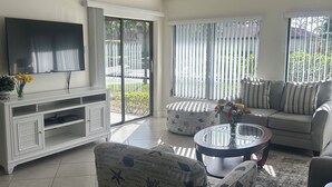 A living room with a TV, sofa, armchair, and a ceiling fan. - Serene retreat awaits at prime location in charming Timberwoods/Village des Pins (Sarasota)