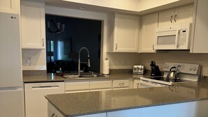 A modern kitchen with white cabinetry, a granite countertop, a stainless steel sink, a microwave, a kettle, and a dishwasher. - Serene retreat awaits at prime location in charming Timberwoods/Village des Pins (Sarasota)