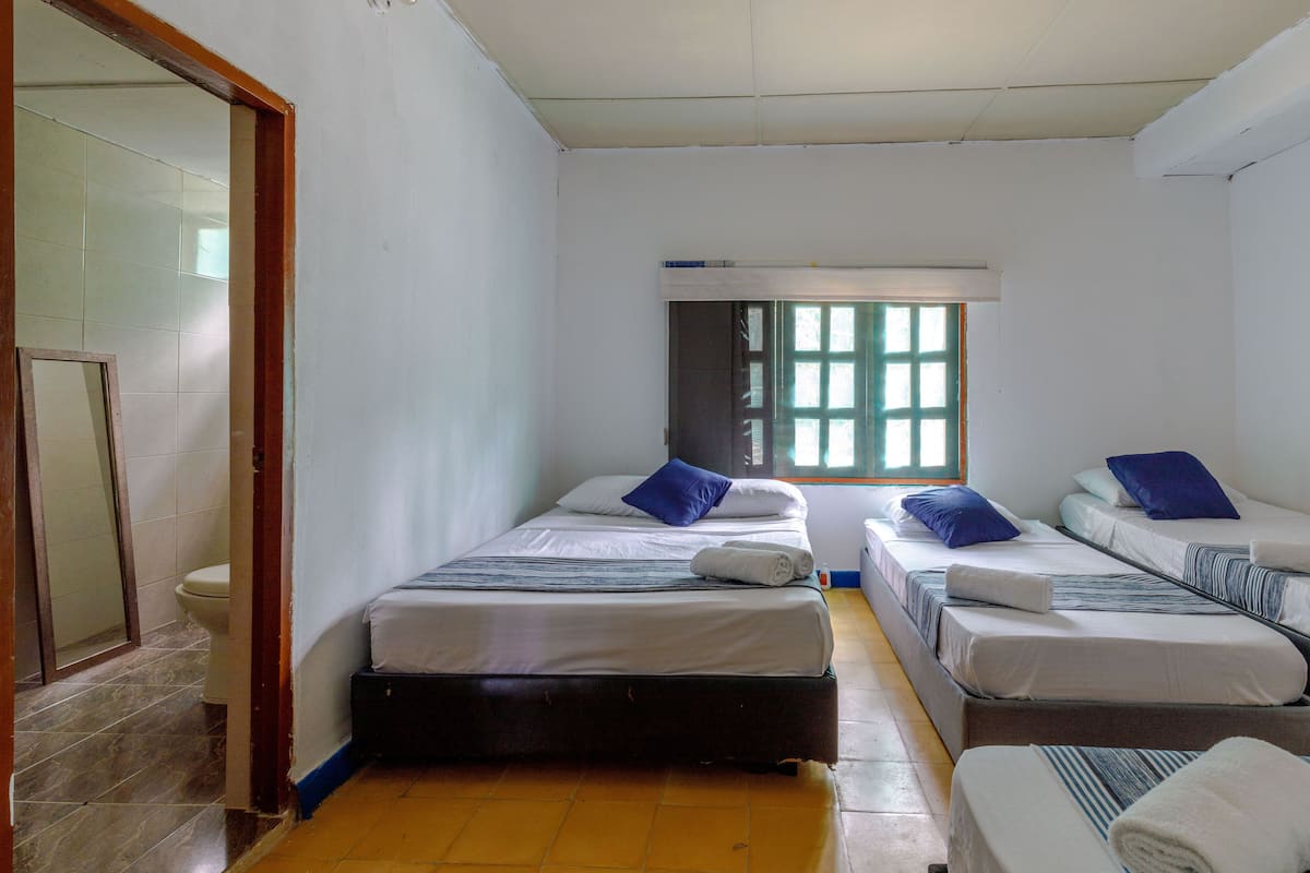 A room with three beds, a window, and a door leading to a bathroom.