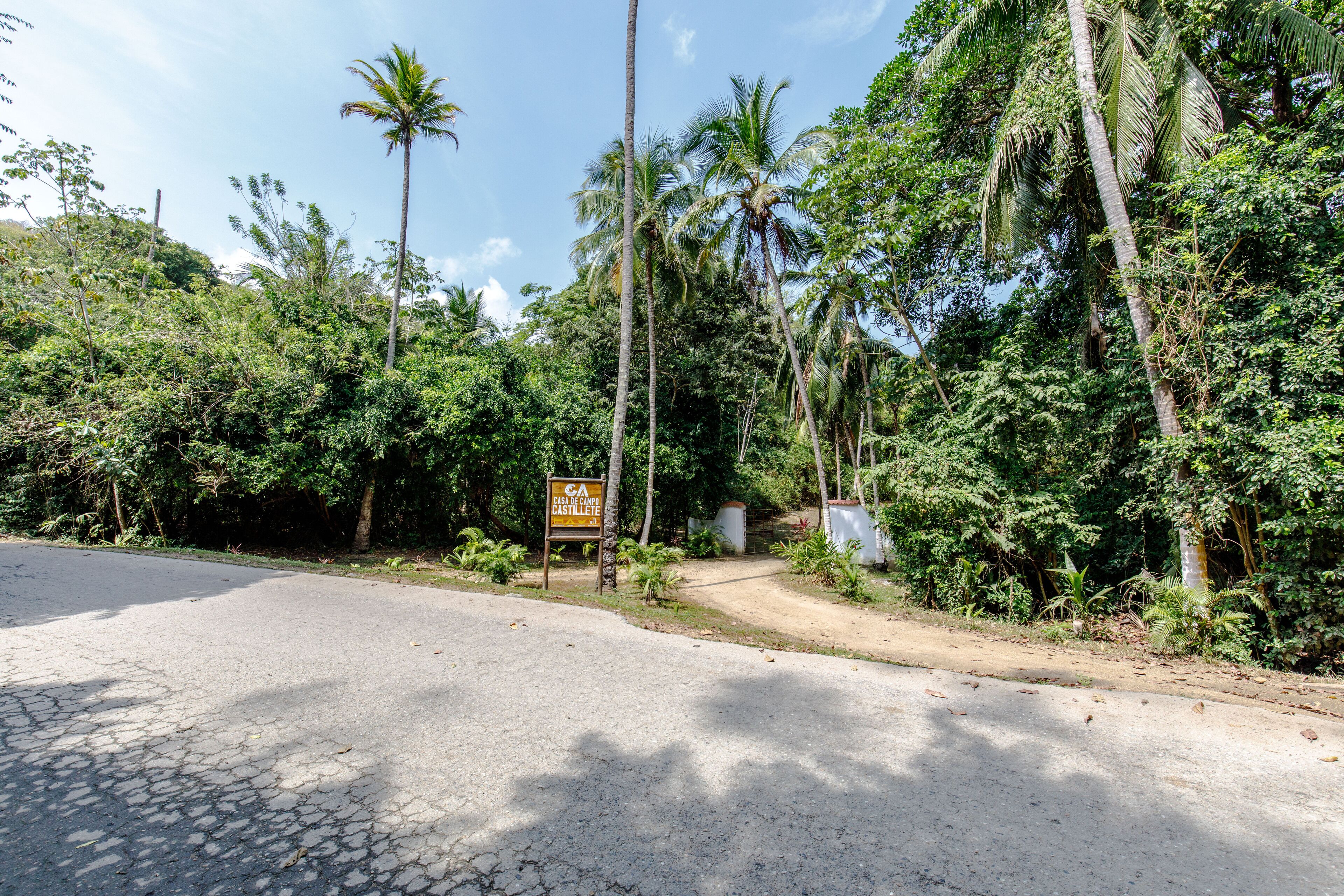 A paved road with a dirt path leading to a signboard.