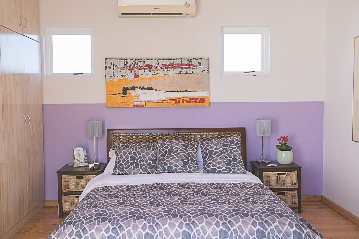 A bedroom with a bed, two nightstands, a wall-mounted air conditioner, and two windows.