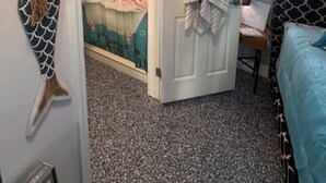 Une chambre avec un lit, une porte sur laquelle est accrochée une serviette, un mur décoré d’une queue de sirène et une affiche sur le mur.