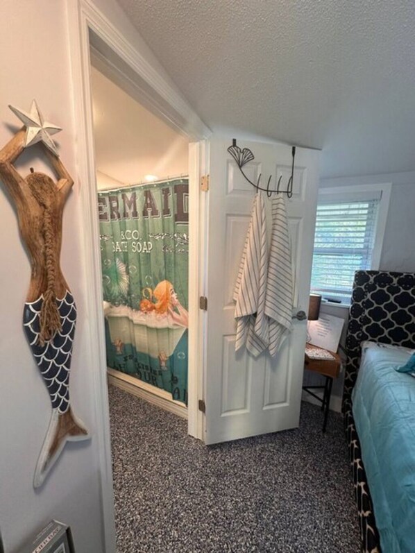 Une chambre avec un lit, une porte sur laquelle est accrochée une serviette, un mur décoré d’une queue de sirène et une affiche sur le mur.