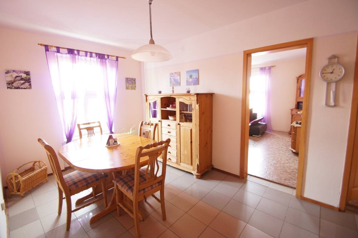 Uma sala de jantar com mesa e cadeiras de madeira, um armário e um relógio na parede.
