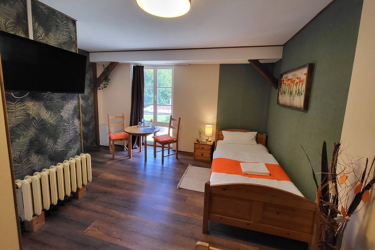 Um quarto com uma cama, uma mesa com cadeiras, um radiador, uma janela com cortinas e um quadro na parede.
