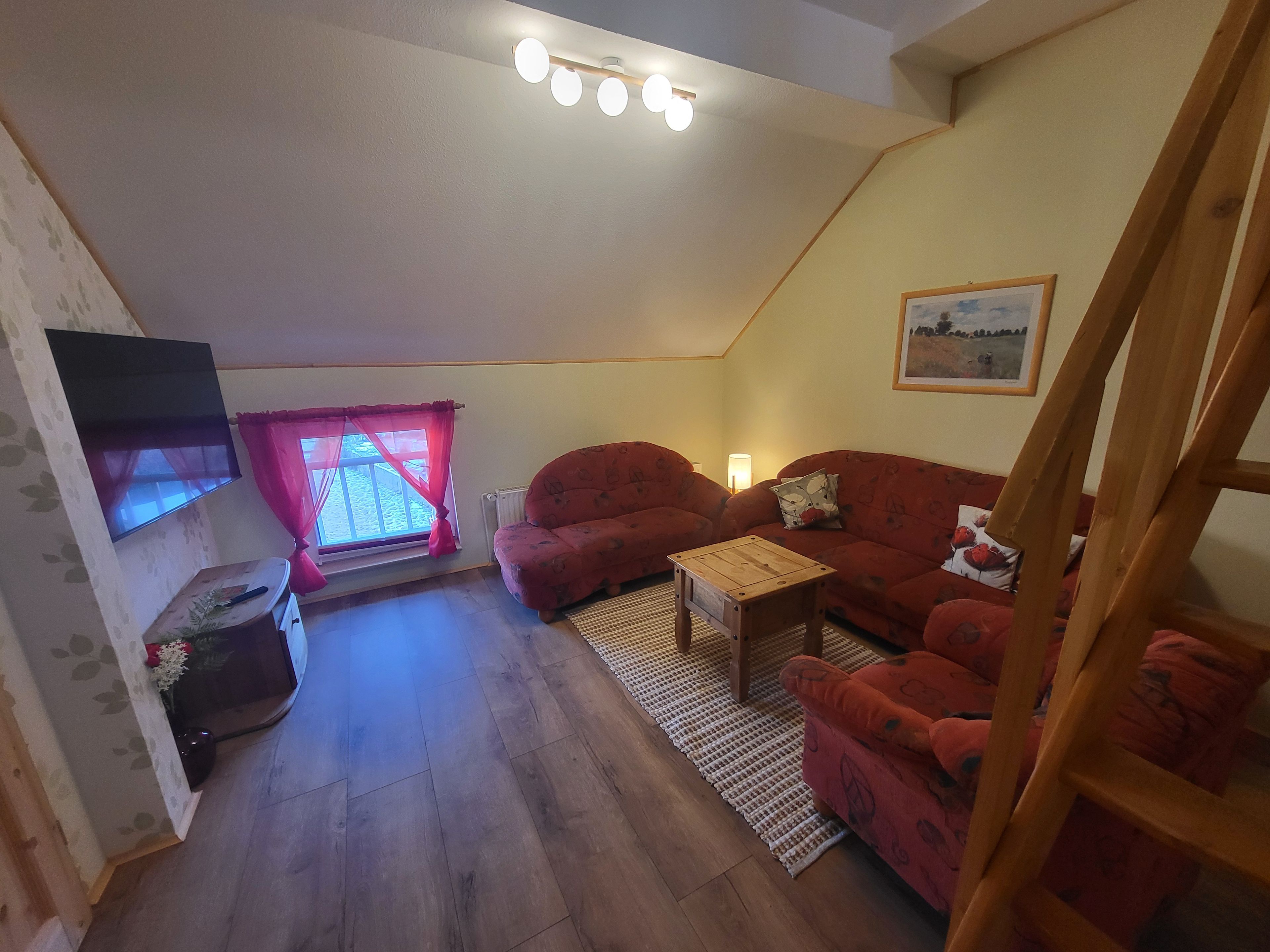 Un salon chaleureux avec un canapé rouge, une table basse en bois et un téléviseur à écran plat fixé au mur.