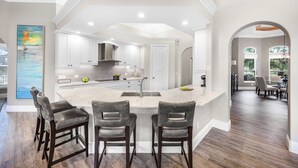A modern kitchen with a central island, bar stools, and a dining area with a view.