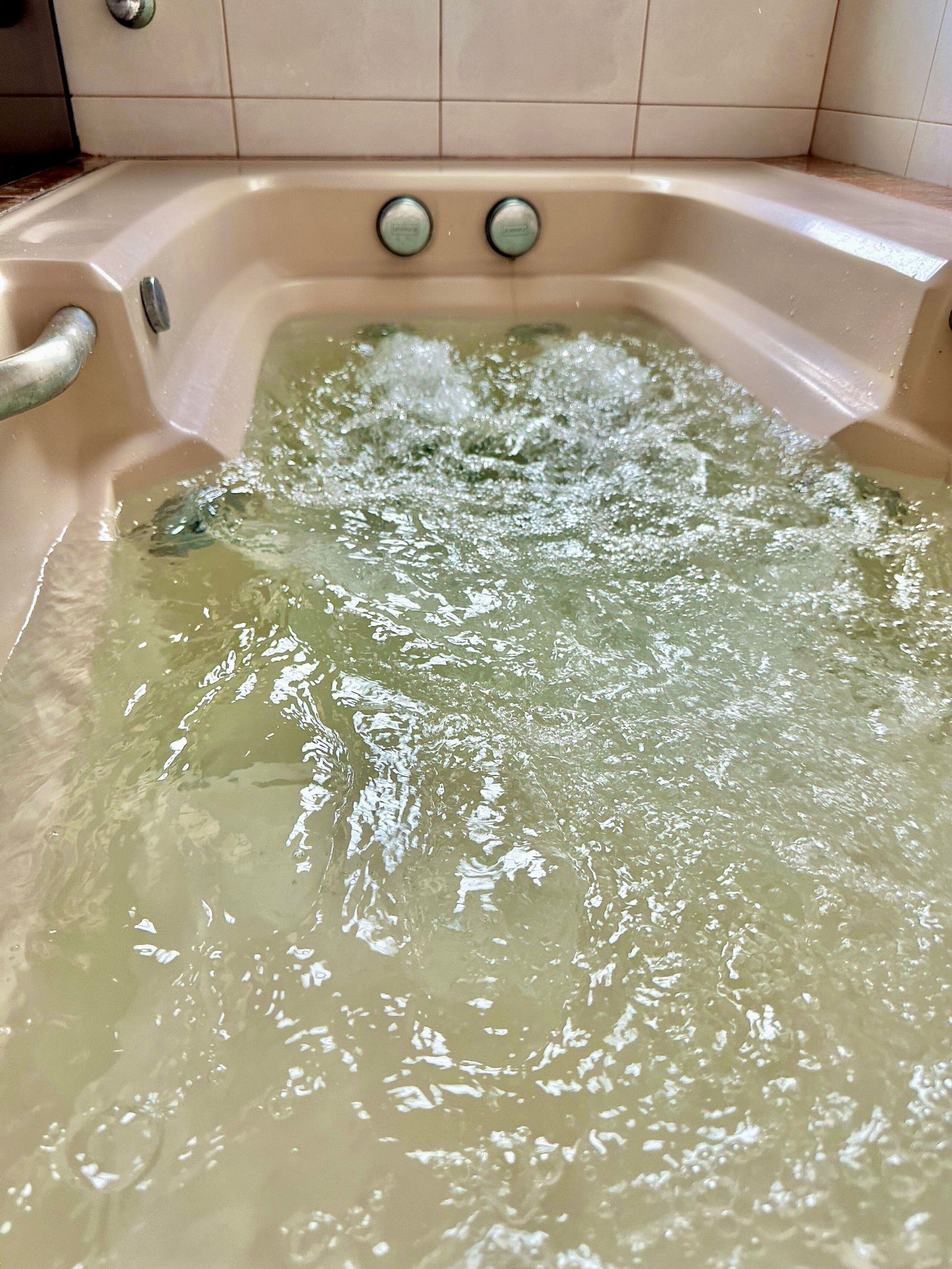 A bathtub with running water and two control knobs.